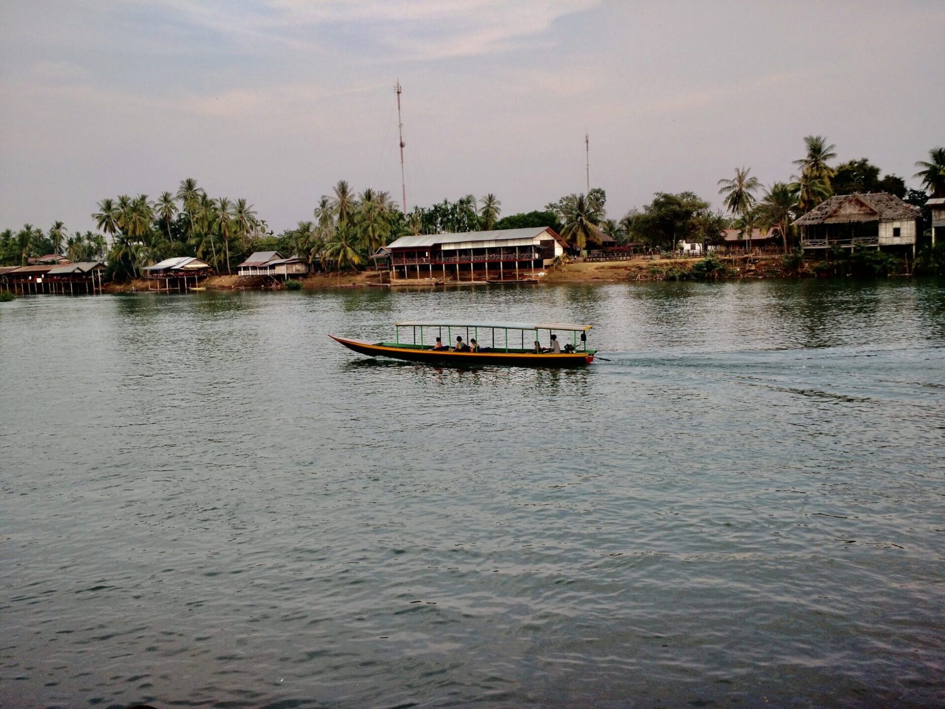 A small wooden boat floating along the river lined with wooden shacks