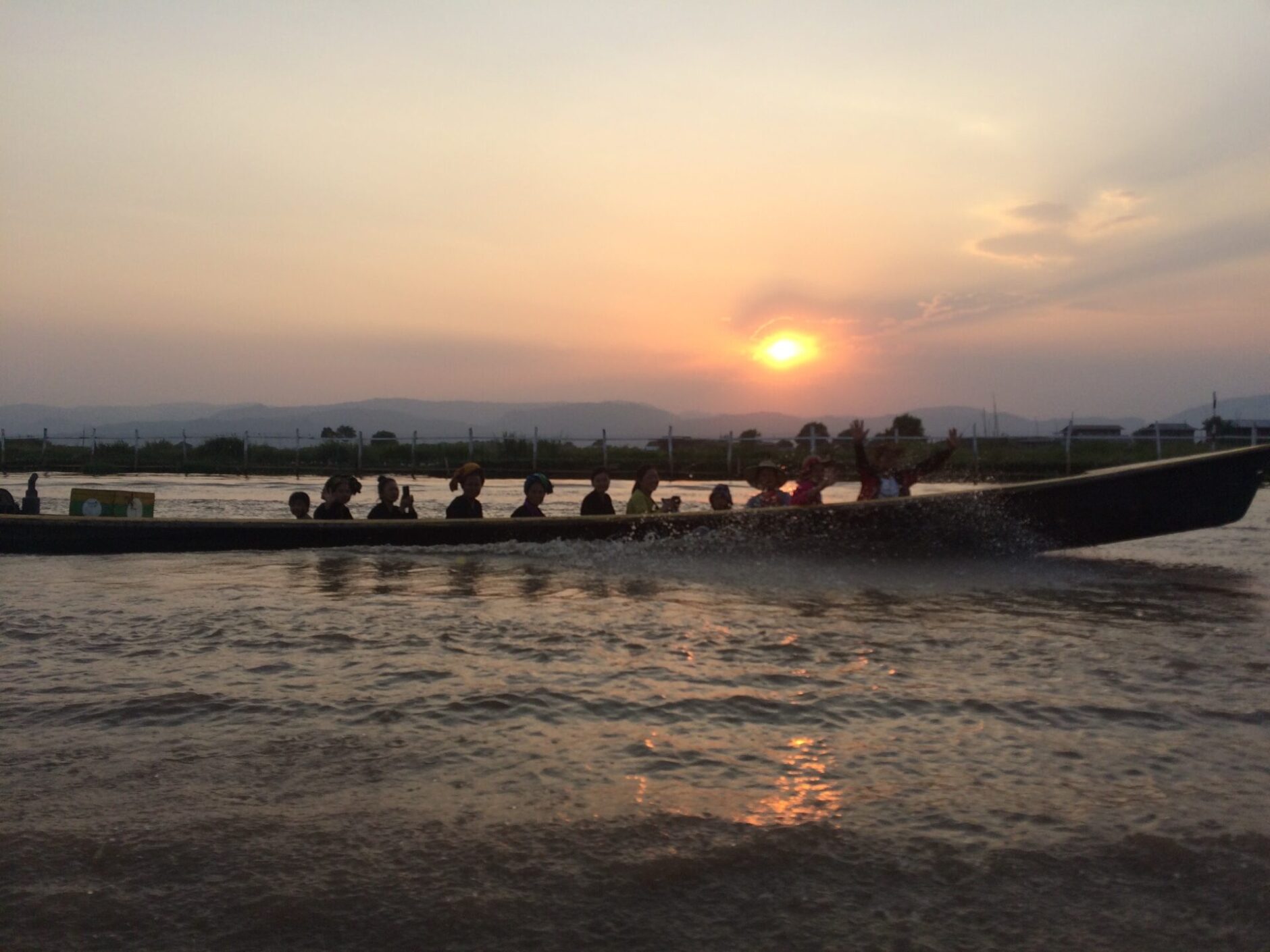 People sitting in a canoe with a yellow sun setting in the background
