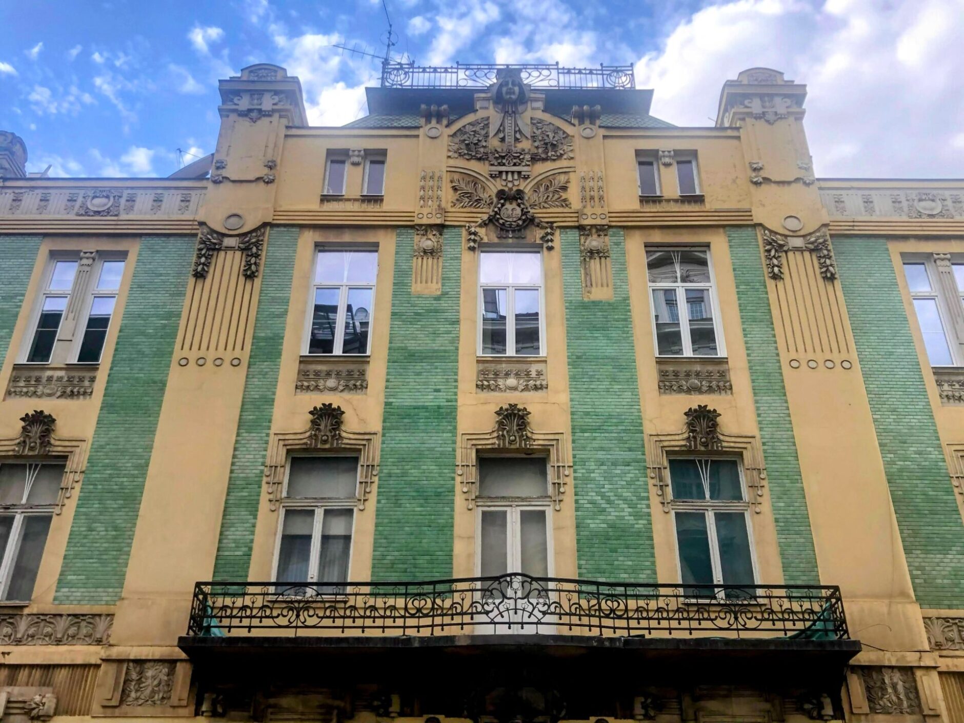 Yellow brick Art Deco building decorated with green tile columns and a long black iron balcony