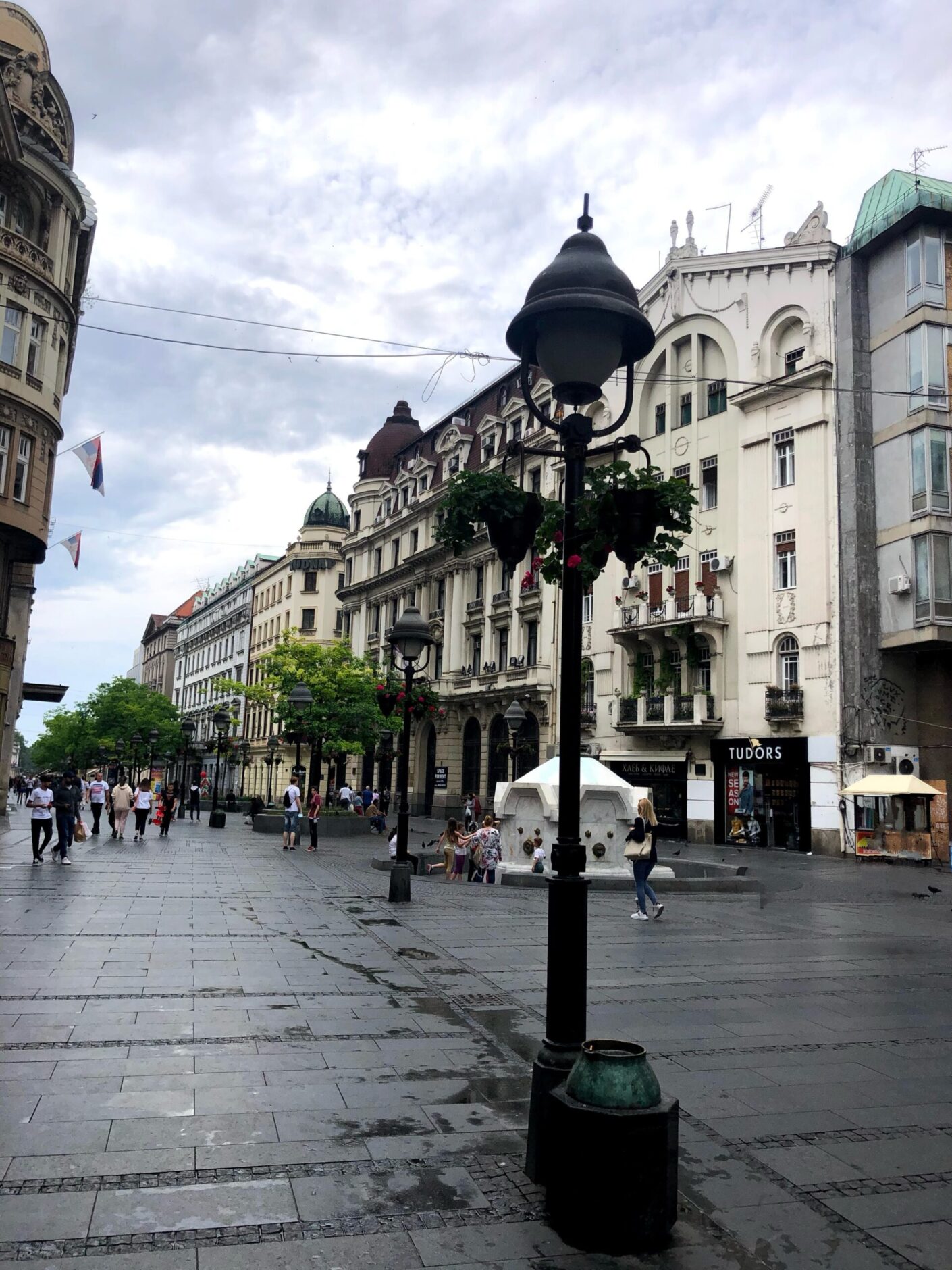 People shopping on pedestrian street lined with Neo-classical buildings and black lamp posts in the middle
