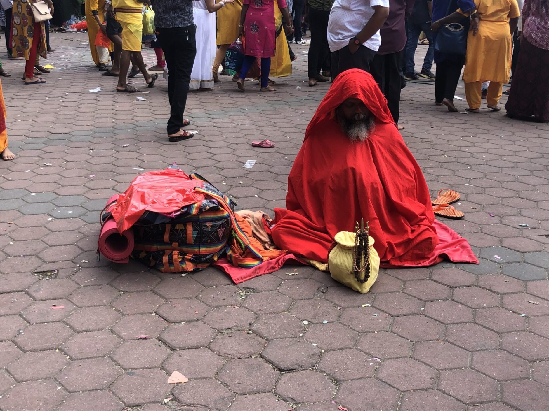 Old man draped in a red cape sitting on the ground