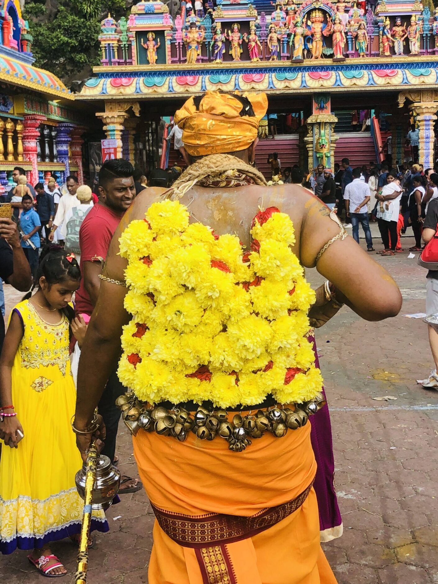 Tall man wearing a yellow turban with rows of yellow marigolds hooked on his back