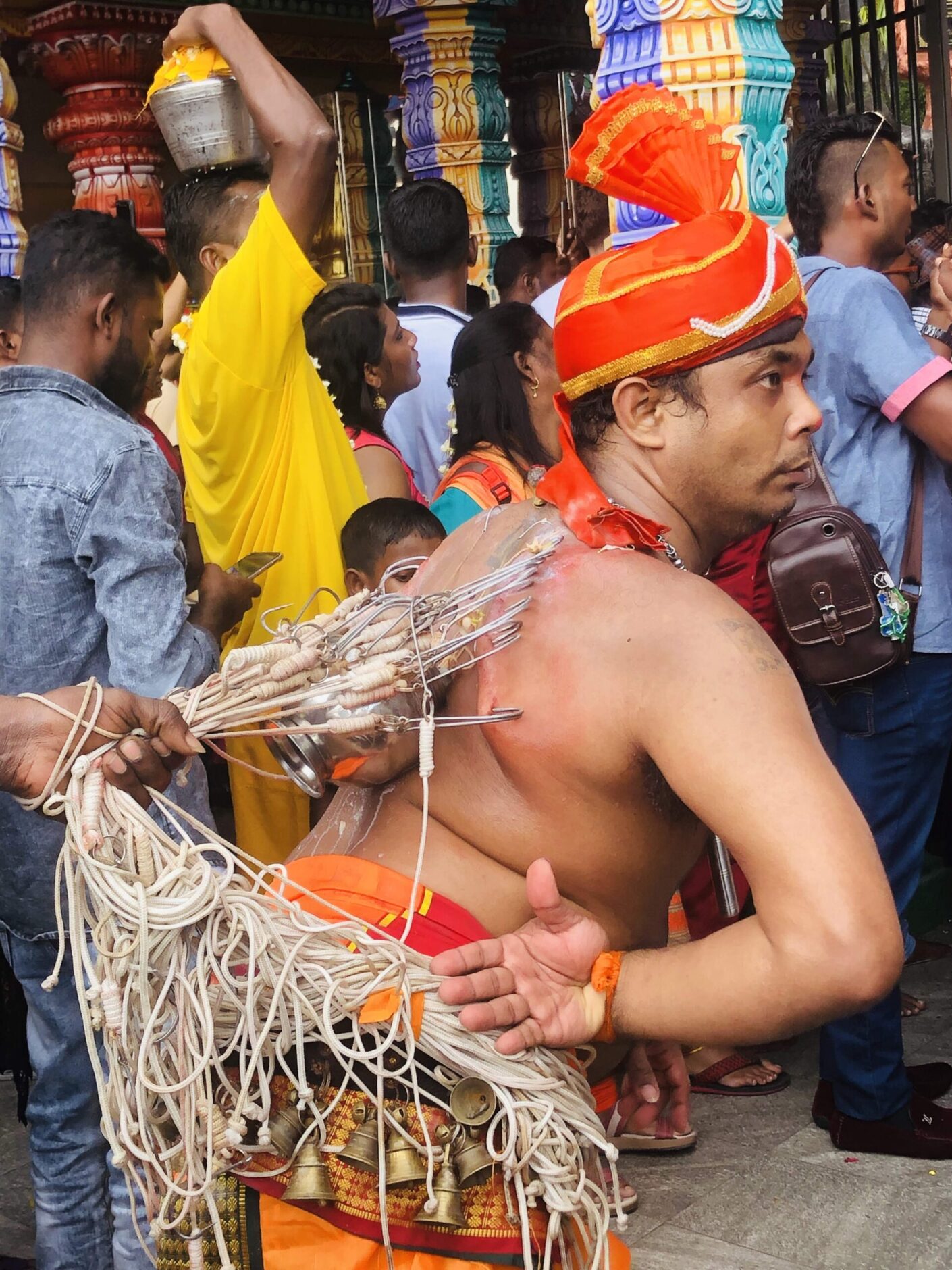 Dancing man wearing an orange turban with hooks entrenched in his back