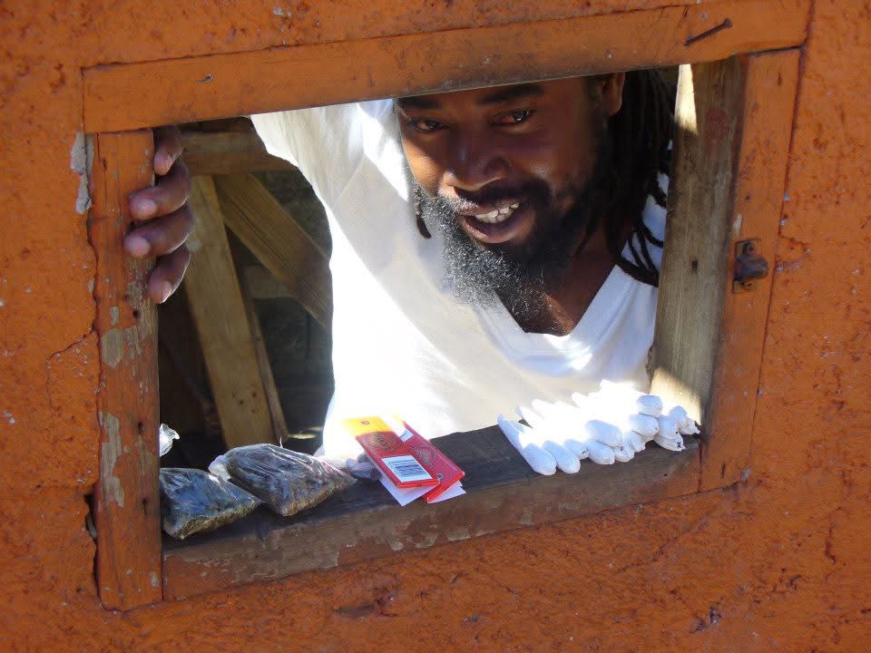 Rastafarian man selling bags of weed through a small square opening of an orange wall at the Bob Marley Mausoleum in Jamaica