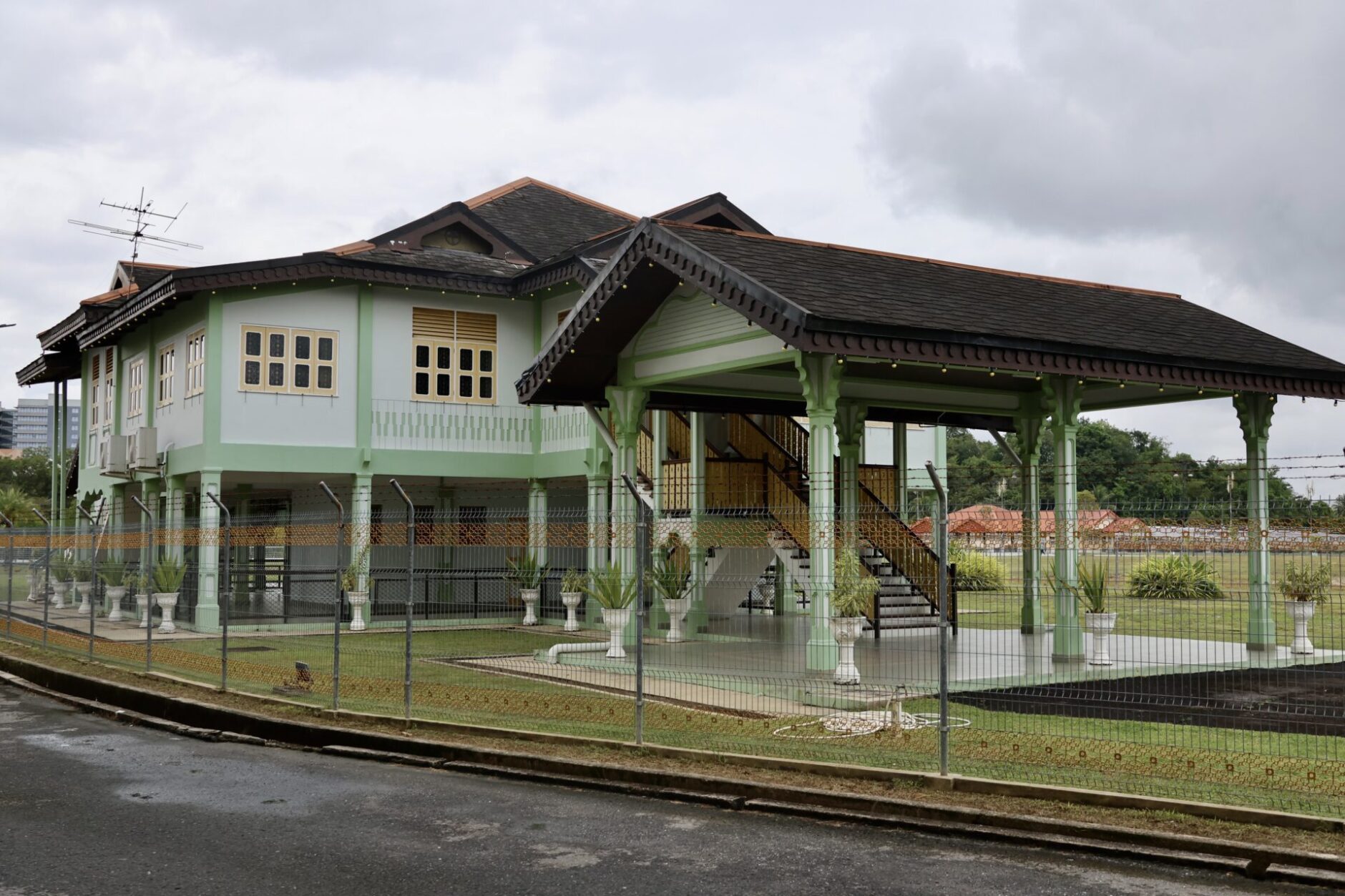 A spacious green house enclosed by a white picket fence, set against a clear blue sky. 