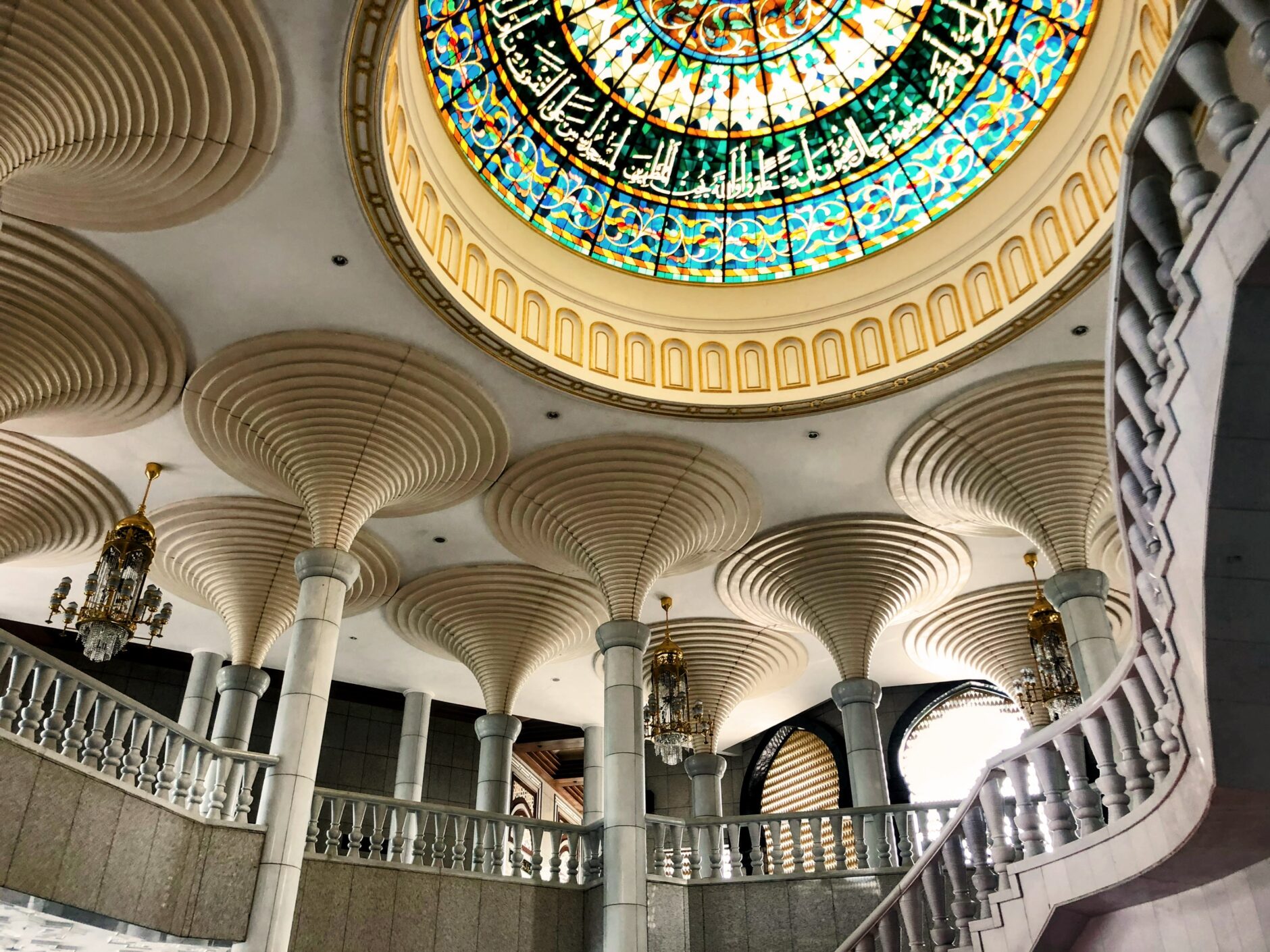 A circular dome in a mosque topped with a stained glass window, casting colorful patterns onto the space below