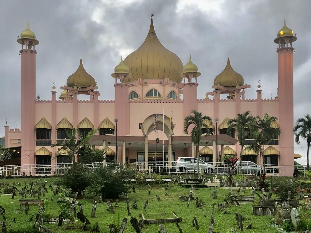 Pink mosque with spiral towers and a grassy cemetary in front