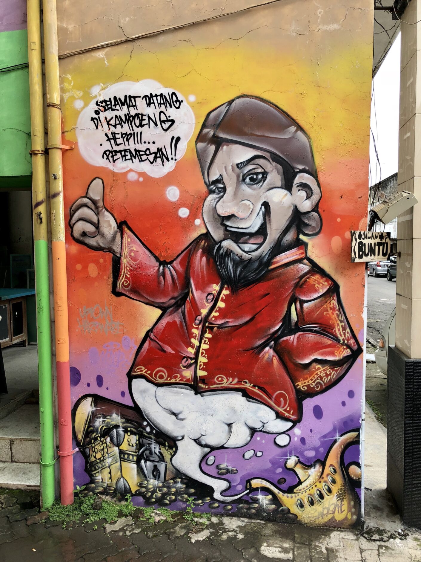 Mural of a smiling Arabic man wearing a brown turban, a red shirt and white pants