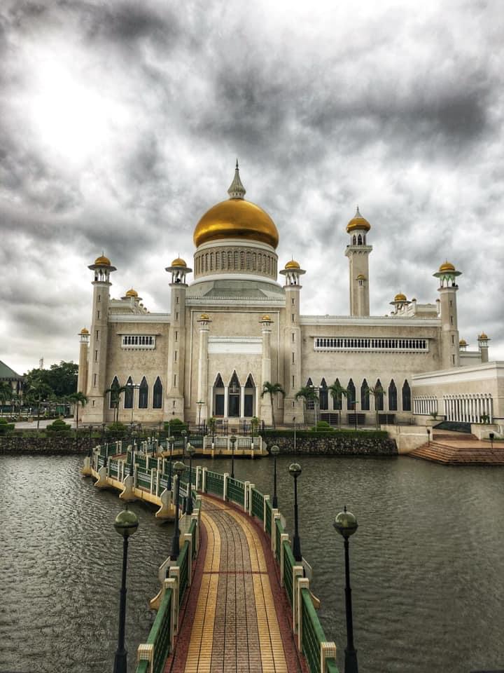 A stunning white and gold mosque stands gracefully on the water, reflecting its beauty in the calm surface below